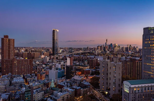 Alacakaranlıkta şehrin yüksek görüntüsü. Şehir merkezindeki apartmanlar ve nehrin üzerindeki köprüye yakın Manhattan Meydanı 'ndaki modern yüksek binalar. Manhattan, New York City, ABD.