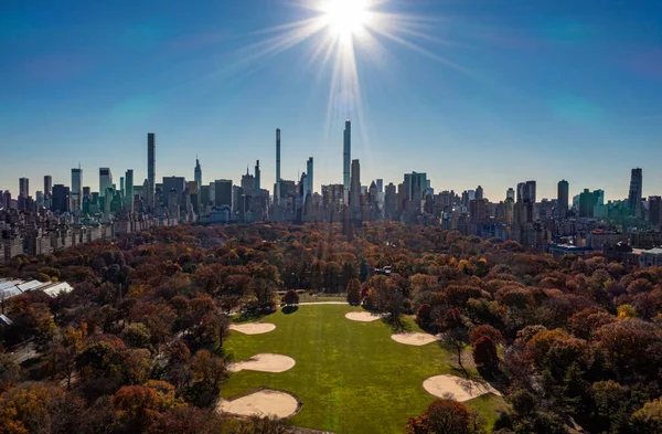 Central Park 'ta sonbaharın geniş panoramik görüntüsü ve güneş ışığına karşı yüksek binaların çevresi. Manhattan, New York City, ABD.