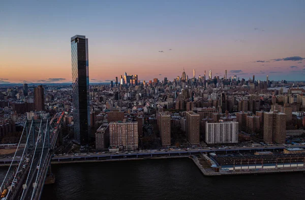 Alacakaranlıktaki muhteşem şehir manzarası, uzaktan aydınlatmalı gökdelenler. Köprü ve rıhtımda yoğun yollar var. Manhattan, New York City, ABD.