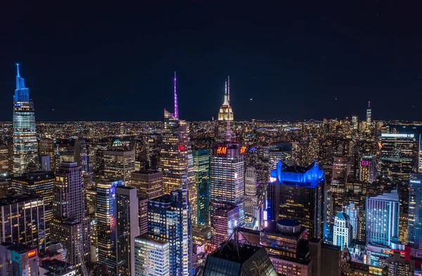 Night city scene of tall downtown skyscrapers in metropolis. High rise buildings with colour illuminated spires on tops. Manhattan, New York City, USA.