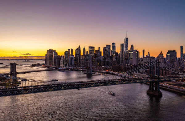 Large cable stayed bridges spanning East River. Skyline with downtown skyscrapers against romantic colourful sunset sky. Manhattan, New York City, USA.