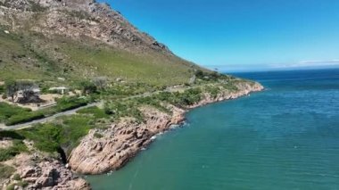 Fly along sea coast in tropical destination. Step rocky slope rising from turquoise water on sunny day. South Africa.