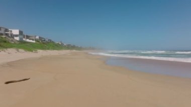 Kumsalın üzerinde alçak uçuş. Yükselen dalgalar tatil bölgesinde kıyıya vuruyor. Güney Afrika.