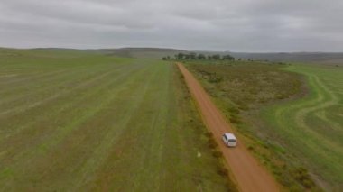 Forwards tracking of passenger minivan driving alone on dirt road in countryside. Aerial view of car in landscape. South Africa.