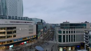Çok katlı ve çeşitli dükkanları olan binalarla çevrili geniş yaya bölgesi. Alacakaranlıkta Zeil alışveriş sokağının üzerinde ilerliyorlar. Frankfurt am Main, Almanya.
