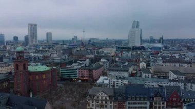 Hava kararırken şehir merkezindeki eski binaların ve kiliselerin üzerinden ileriye doğru uçuyorlar. Arka planda modern binalar. Frankfurt am Main, Almanya.
