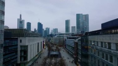 Forwards fly around shopping galleries along Zeil street in city centre. Revealing cityscape with downtown skyscrapers at dusk. Frankfurt am Main, Germany.