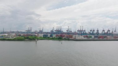Forwards fly above water surface. Staked overseas containers in port. High harbour cranes in background. Global logistics and transportation. Hamburg, Germany.