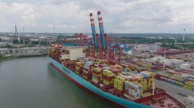 Slide and pan footage on unloading huge container ship in harbour. Logistic terminal in city. Heavy transport on roads in background. Hamburg, Germany.