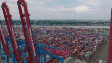Forwards fly above logistic terminal. Rows of colourful stacked naval containers and large cranes. Intermodal transport and global logistics. Hamburg, Germany.