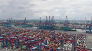 Fly above large logistic areal in harbour. Thousand of containers waiting for delivery to customer. Heavy cranes loading and unloading units from huge overseas cargo ships. Hamburg, Germany.