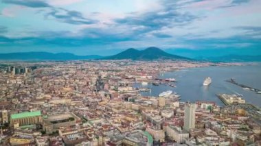 Twilight in coastal city. Forwards fly above famous city with port at sunset. Evening aerial panoramic hyperlapse shot of Naples and Mount Vesuvius massif in distance, Italy.