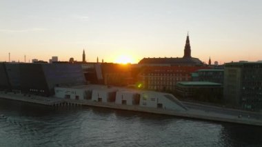 Kanal rıhtımındaki modern ve tarihi binalar gün batımına karşı. Alacakaranlıktaki şehrin hava indirme görüntüleri. Tekne suda yüzüyor. Kopenhag, Danimarka.