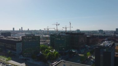 İleri uçaklar şehir merkezinin üzerinde. Modern şehir ilçesinde çok katlı binalar. Gökyüzüne karşı inşaat alanındaki vinçler. Kopenhag, Danimarka.