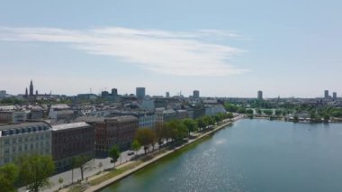 Şehirdeki güneşli bir günde göl kenarındaki yolda giden araçların izini sürüyorum. Hava sineması görüntüleri. Kopenhag, Danimarka.