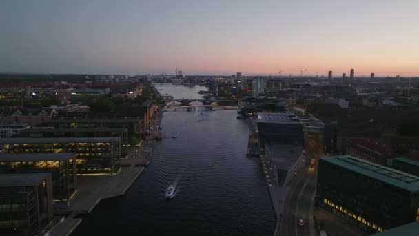 前方の水の運河の上の夜の都市で飛ぶ 水辺のモダンなデザインの建物 夕暮れの空に対する資本の空中ビュー デンマークのコペンハーゲン — ストック動画