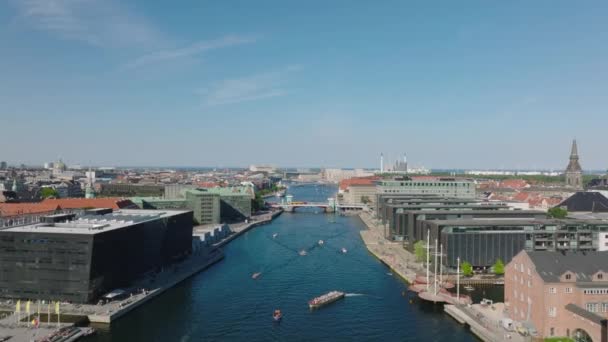 転送市内の水の運河の上を飛ぶ ウォーターフロントの近代的な建物に沿って水面を通過するボート 首都の晴れた日 デンマークのコペンハーゲン — ストック動画