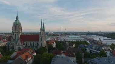 Alacakaranlıktaki gotik kilisenin hava yükselen görüntüleri. Theresienwiese, Oktoberfest sitesinde büyük bira çadırları ve renkli bir şekilde yanıp sönen gösteriler. Münih, Almanya.
