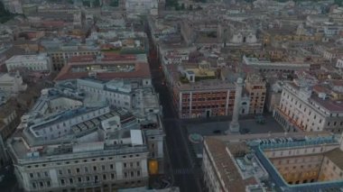 Şehirdeki apartmanların tepesindeki terasların üstünde alçak uçuş. İleriye doğru yükselen güneşe karşı uçar. Roma, İtalya.