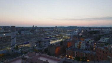 Aydınlatılmış merkez tren istasyonunun renkli alacakaranlık gökyüzü altında havadan görünüşü. Şehirdeki konut binalarının kayarak ifşası. Roma, İtalya.