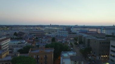 İleri, yerleşim bölgesinin üzerinden uçar. Alacakaranlıkta şehrin aydınlık binaları, renkli alacakaranlık gökyüzü. Roma, İtalya.