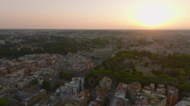 Gün batımında şehrin tarihi simgelerinin havadan görüntüsü. Ünlü Colosseum amfitiyatrosu ve Oppian Tepesi 'ndeki parktaki antik anıtlar. Roma, İtalya.