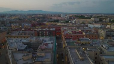 Alacakaranlıkta şehrin dışındaki apartmanların üzerinde ilerliyorlar. Dağ sırtı silueti uzakta. Roma, İtalya.