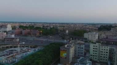 Tren raylarında yavaşça hareket eden yolcu treni. İlerideki binalar üzerinde uçuyor. Şehir merkezindeki demiryolu boyunca. Gün batımında. Roma, İtalya.