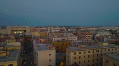 Alacakaranlıkta şehir merkezindeki binaların çatısının üstünde alçak uçuş. Şehirde çeşitli konutlar var. Roma, İtalya.
