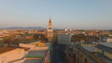İleri doğru çanlar eşliğinde tarihi kule etrafında uçar. Şehir merkezindeki binalar altın saat. Roma, İtalya.