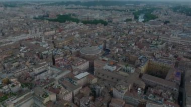 Modern renkli bina ile yeşil ağaçlı büyük mezarlık arasında giden çok şeritli yolda giden arabaların havadan yükselen görüntüleri. Doğan güneşe karşı görüş. Roma, İtalya.