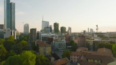 Gün batımında şehir merkezindeki apartmanların üzerinden uçuyor. Uzakta modern yüksek iş kuleleri. Milano, İtalya