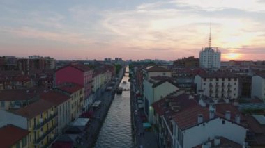Naviglio Grande turistik merkezinin üzerinden geriye doğru uçuyor. Kanaldaki su yüzeyi renkli günbatımı gökyüzünü yansıtıyor. Milano, İtalya.