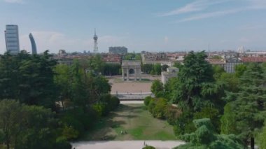 İleri, parkın üzerinde uçar. Arco della Pace 'in hava görüntüleri ve arka planda şehir merkezindeki binalar. Milano, İtalya.