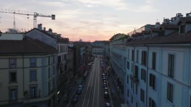 Forvetler caddenin üzerinde ve Porta Cenova mahallesindeki binalar üzerinde uçuyor. Renkli günbatımına karşı şehir manzarasının yükselişi. Milano, İtalya.