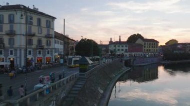 Darsena 'nın su yüzeyinin üzerinden uç. Renkli gökyüzünü yansıt. Alacakaranlıkta rıhtımdan geçen tramvayın izini sürüyorum. Milano, İtalya.