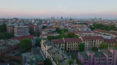 Günbatımında şehir merkezindeki apartmanın üzerinden uçuyor. Uzaktaki modern yüksek katlı ofis binaları. Milano, İtalya.