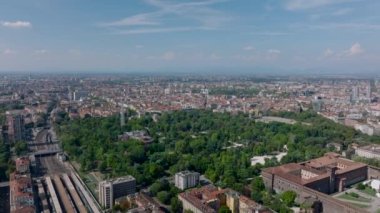 İleri, kasabanın üstünden uçar. Geniş kamu parkındaki yeşil yaprak döken ağaçların ve çevresindeki binaların havadan görünüşü. Milano, İtalya.