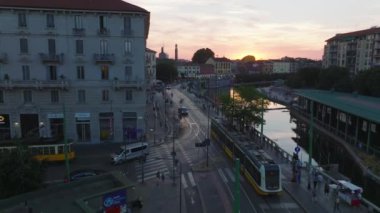 Çağdaş tramvay birimini takip ediyor kavşaklardan geçiyor ve su boyunca araba sürüyor. İnsanlar şehirde günbatımının tadını çıkarıyorlar. Milano, İtalya.