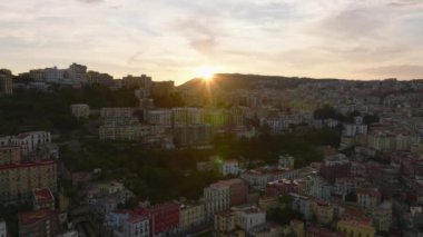 Dik yamaçtaki çok katlı apartmanları renklendirin. Tepenin arkasında batan güneşe karşı şehir manzarası. Napoli, İtalya.