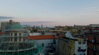 Şehir merkezindeki çatıların üstünde alçak uçuş. İskelelerle kaplı bir kuleyle binanın etrafında uçun. Napoli, İtalya.