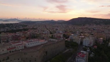 Ortaçağ kalesinin ve şehir merkezindeki binaların havadan görünüşü. Tepeler ve deniz kıyıları uzakta. Renkli alacakaranlık gökyüzü. Napoli, İtalya.