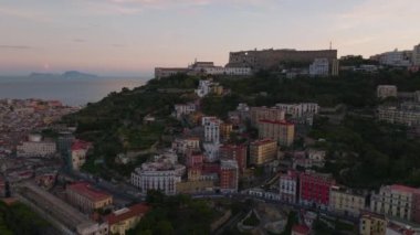 Tepedeki ortaçağ şatosunun ve bayırdaki apartmanların hava kaydırak ve pan görüntüleri. Gün batımında Castel SantElmo. Napoli, İtalya.