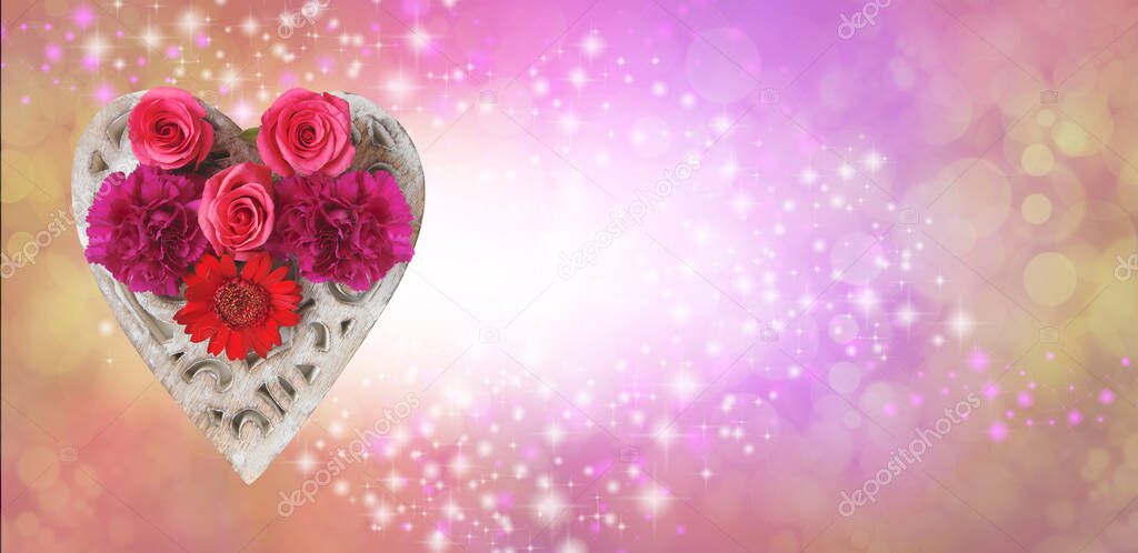 Love and flowers message background - Red pink flower heads arranged on a wooden heart against a peachy pink gold bokeh background with white centre and sparkles providing space for message