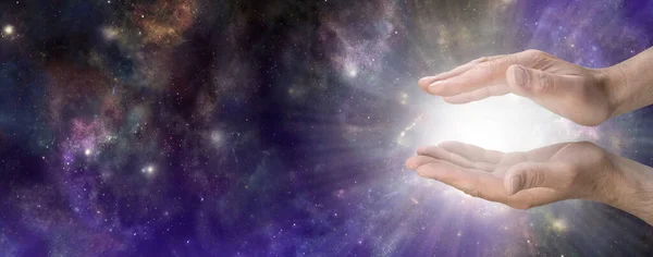 Heavenly Life Force Concept sky Banner - male cupped hands with bright white light energy radiating outwards against wide dark celestial deep space  sky background with copy space