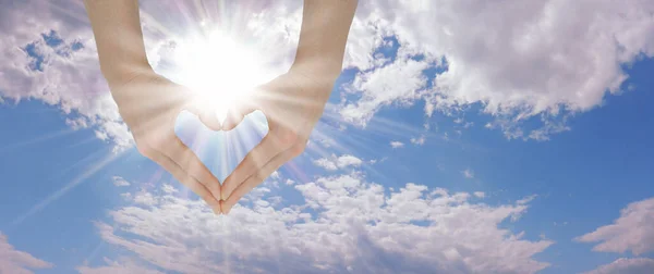 Heart Hands and Summer Sky background - blue sky and fluffy clouds with a beautiful bright sun above female hands making a heart shape and copy space