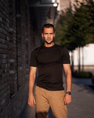 Binanın arka planında siyah tişörtlü kısa tüylü yakışıklı bir adam.