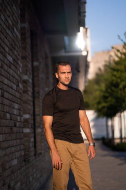 Binanın arka planında siyah tişörtlü kısa tüylü yakışıklı bir adam.