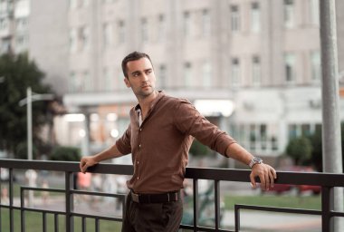 Şehir caddesinde kahverengi gömlekli, tıraşsız, genç bir adamın portresi.