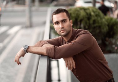 Şehir caddesinde kahverengi gömlekli, tıraşsız, genç bir adamın portresi.